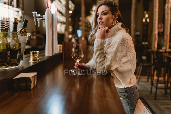 Stylish thoughtful woman drinking wine at counter in bar — Stock Photo
