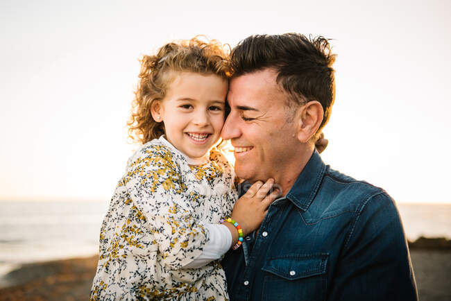 Homem de meia idade com sua filha na costa do mar sorrindo e abraçando uns aos outros — Fotografia de Stock