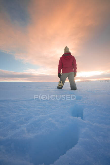 Turista em roupas quentes em pé no majestoso campo nevado no fundo do céu brilhante por do sol — Fotografia de Stock