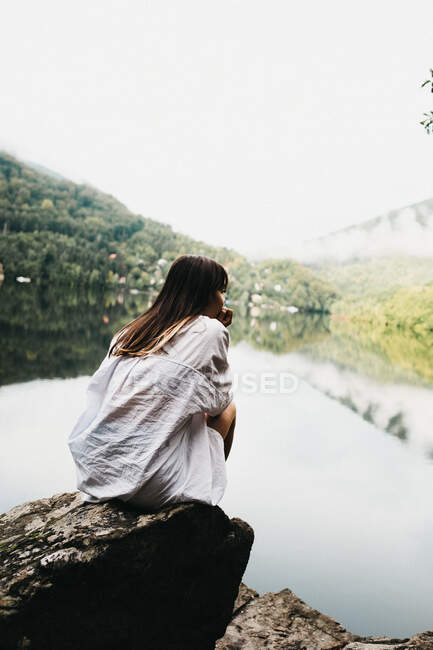 Frau sitzt auf Felsen in der Nähe von See und Bergen — Stockfoto