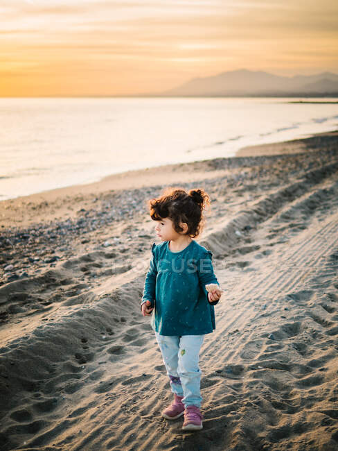 Маленькая девочка, стоящая у пляжа на песке и смотрящая на море — стоковое фото