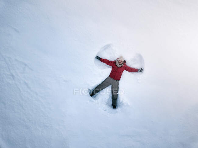 Зверху усміхнений чоловік середнього віку в одязі лежить на білому снігу і робить силует снігового ангела — стокове фото