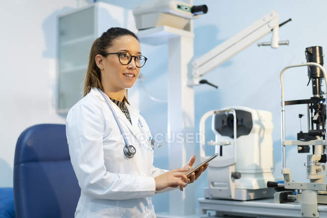 Young smiling female doctor in uniform using using smartphone in room — Stock Photo