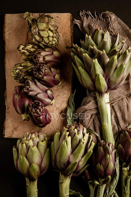 Fresh ripe artichokes with napkin on brown wooden table — Stock Photo