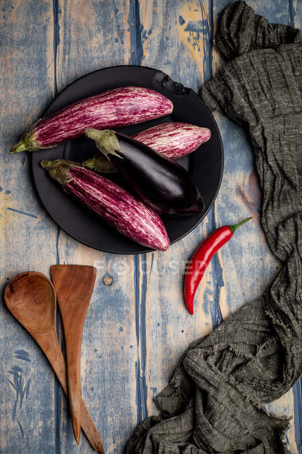 Fresh ripe eggplants on plate with chilli pepper on weathered wooden tabletop — Stock Photo