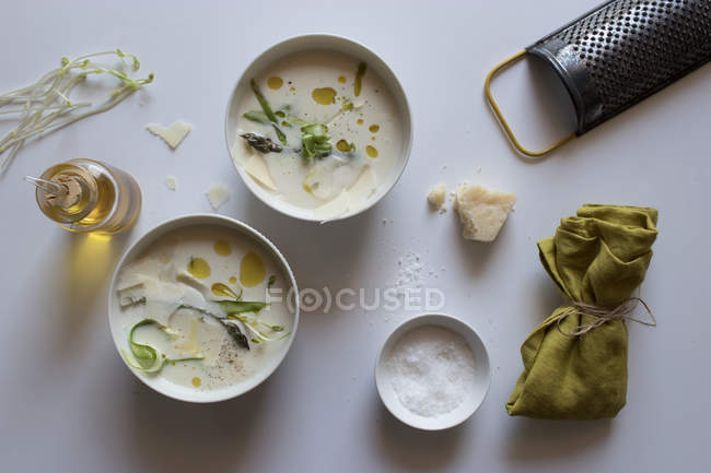 Tazones de deliciosa sopa de crema de espárragos con queso y hierbas sobre fondo blanco - foto de stock