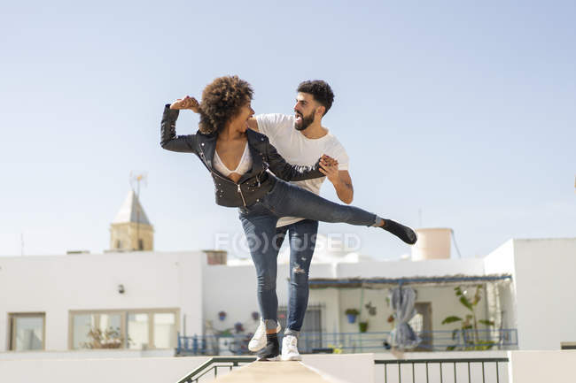 Multiracial homem e mulher rindo e equilibrando na parede enquanto se divertindo na rua da cidade durante a data — Fotografia de Stock