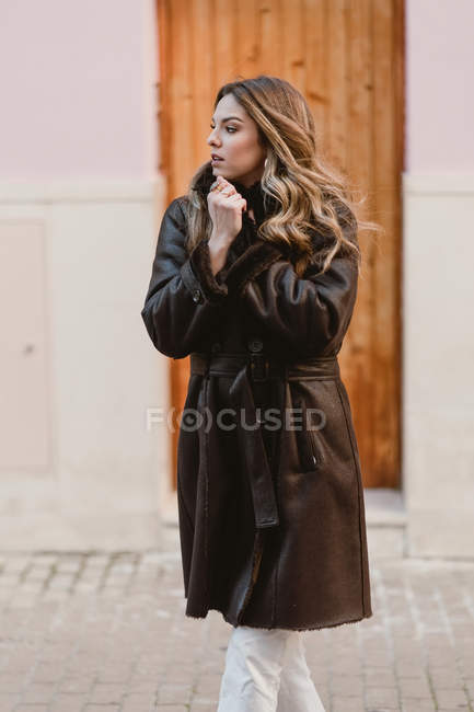 Stylish woman in vintage leather coat standing near wooden door on street — Stock Photo