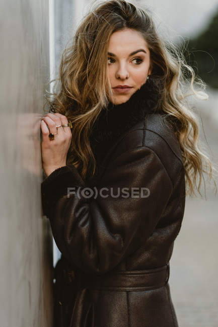 Mulher sensual em casaco de couro em pé na rua e olhando para longe — Fotografia de Stock