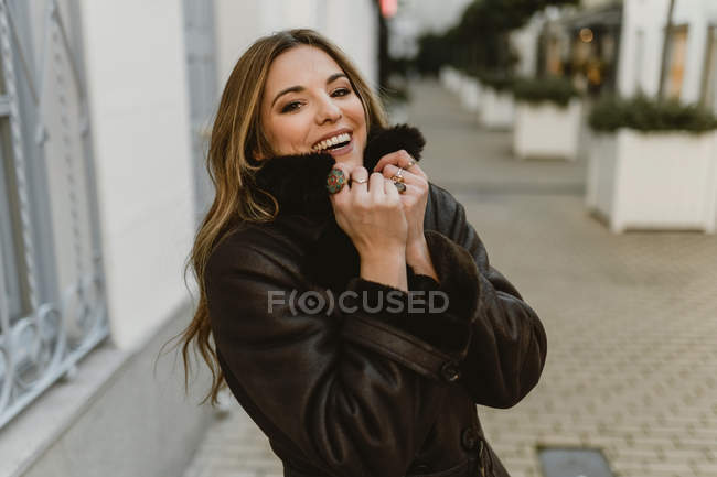 Laughing elegant woman standing on city street and looking at camera — Stock Photo