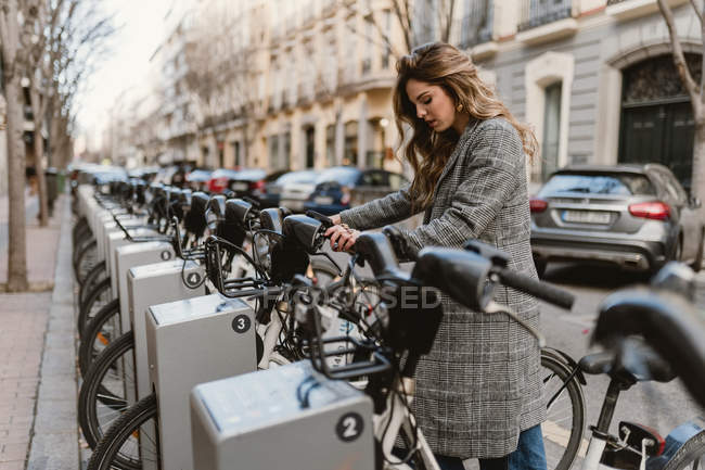 Señora elegir la bicicleta de alquiler en el estacionamiento - foto de stock