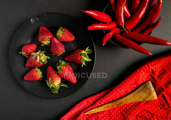 Red fabric and twigs with bright buds placed on black background near hot chili peppers and sweet ripe strawberries — Stock Photo