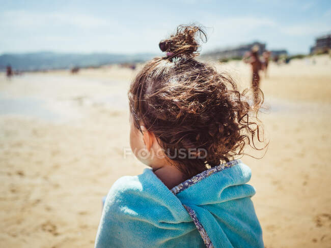 Anonymous little girl from behind standing by the beach on sand looking at the sea — Stock Photo