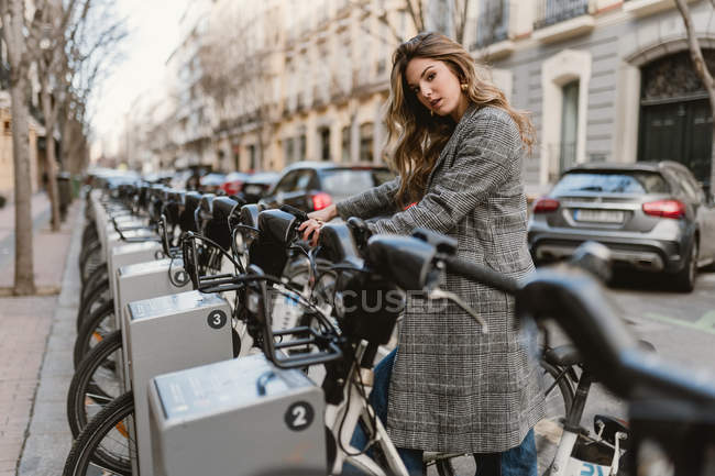 Senhora escolhendo aluguer de bicicleta no estacionamento — Fotografia de Stock