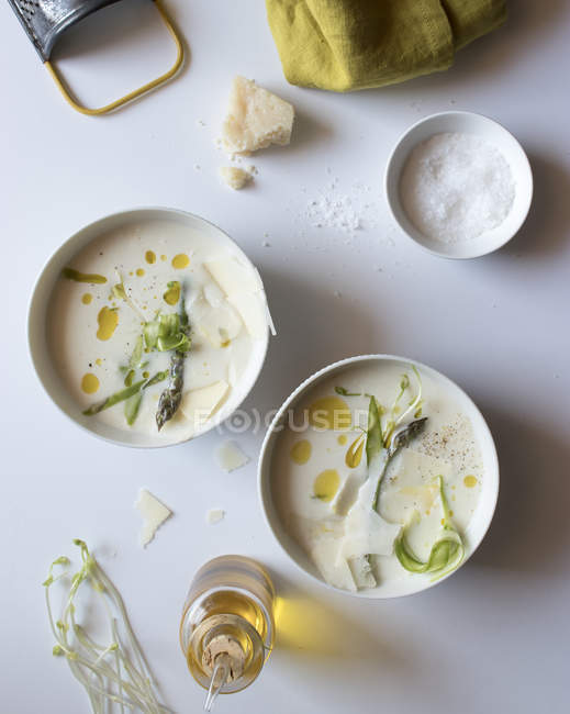 Tazones de deliciosa sopa de crema de espárragos con queso y hierbas sobre fondo blanco - foto de stock