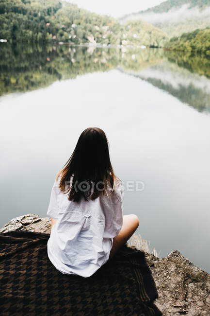 Mulher sentada em cobertor perto do lago e montanhas — Fotografia de Stock