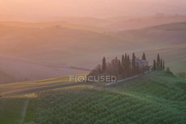 Pintoresco paisaje de campos verdes con casa de campo y árboles en la luz del sol brillante, Italia - foto de stock