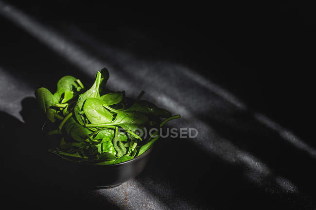 Gesunder frischer Spinat in schwarzer Schüssel auf dunklem Hintergrund — Stockfoto