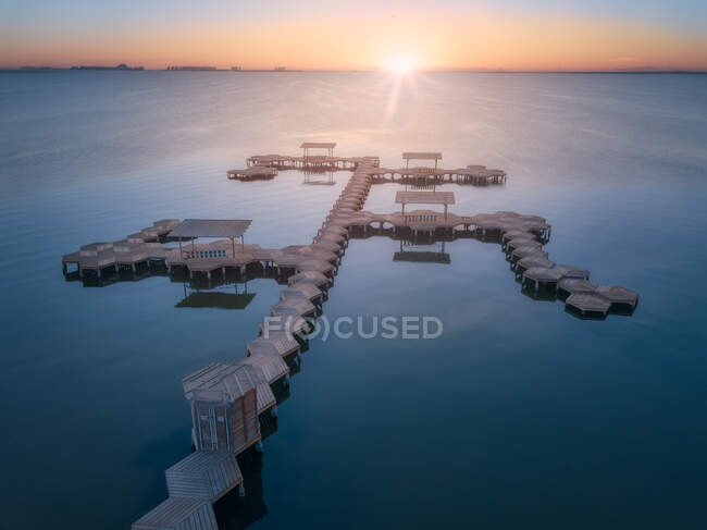 Vista aerea del molo geometrico in legno vuoto sopra l'acqua tranquilla su sfondo tramonto luminoso — Foto stock