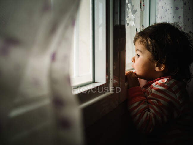 Menina pequena olhando através da janela em casa — Fotografia de Stock