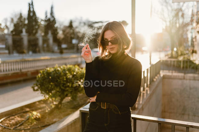 Stylish woman smoking cigarette near metro station on sunny street — Stock Photo