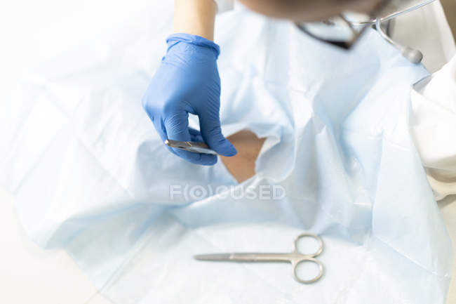 Doctora en uniforme y máscara médica sacando puntos de sutura del paciente en servilleta - foto de stock