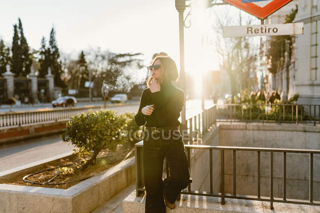 Stylish woman lighting cigarette near metro station in city — Stock Photo