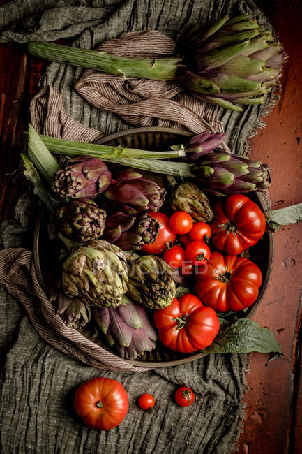 Bowl of various fresh vegetables and cloth napkins on rustic table in kitchen — Stock Photo