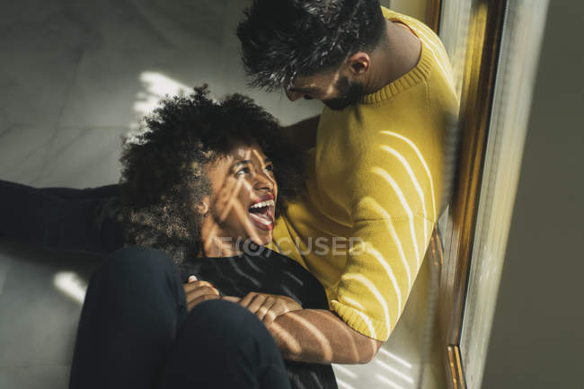 Bastante alegre mujer afroamericana riendo mientras está acostado en las rodillas del hombre barbudo en el suelo - foto de stock