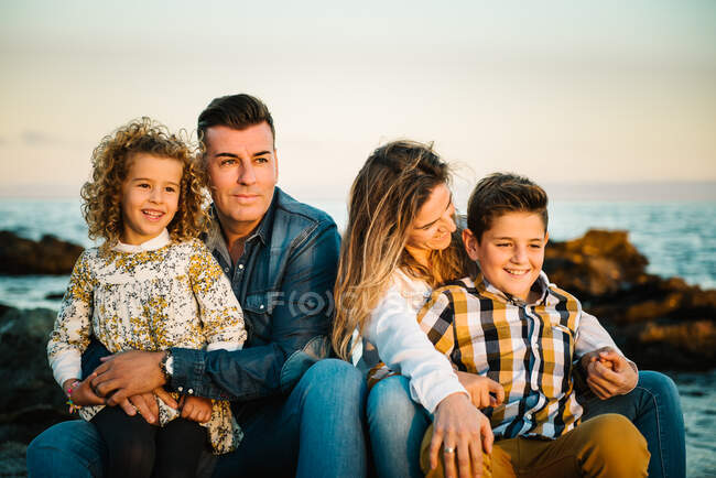 Мужчина средних лет женщина с детьми на берегу моря улыбается и обнимает друг друга — стоковое фото