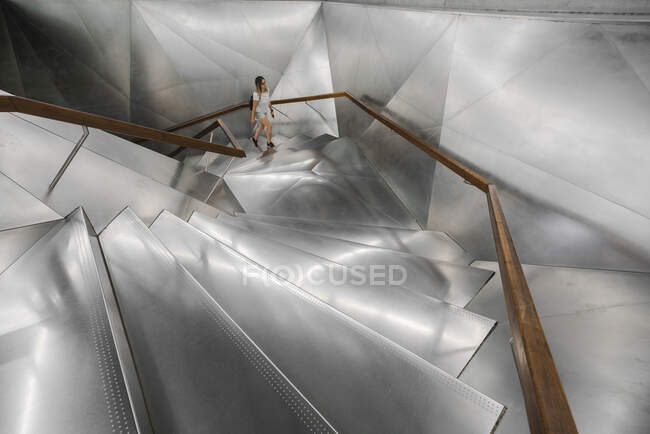 Mulher casual andando escadas modernas incríveis com passo de aço brilhante e corrimão de madeira — Fotografia de Stock
