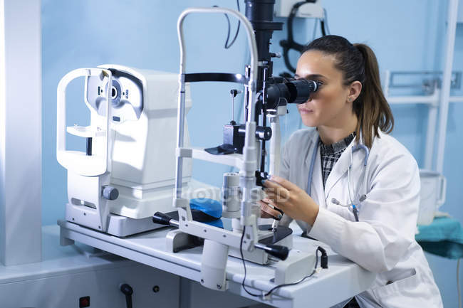 Молода жінка-медик використовує мікроскоп на робочому місці на розмитому фоні — стокове фото
