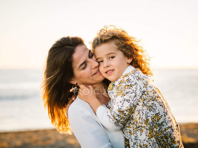 Жінка середнього віку з дочкою на морському березі посміхається і обіймає один одного — стокове фото