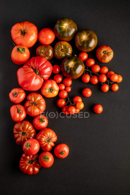 Pomodori freschi maturi assortiti sparsi sulla superficie nera — Foto stock