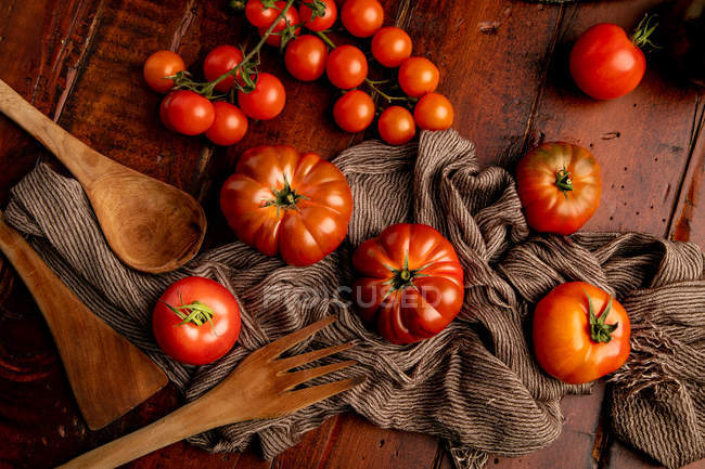Assorted fresh tomatoes and fabric napkin on lumber tabletop in kitchen — Stock Photo