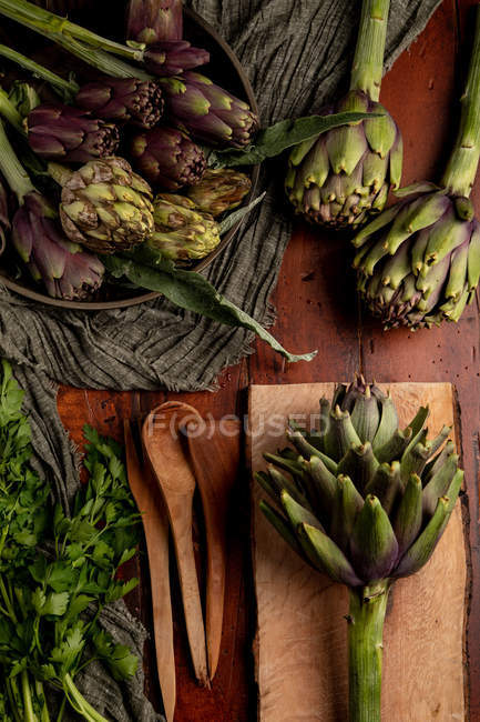 Artichauts frais mûrs et persil sur plateau en bois — Photo de stock