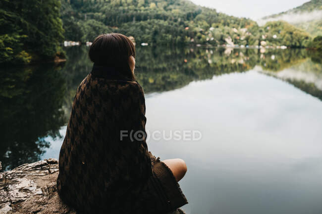 Femme assise avec couverture près du lac et des montagnes — Photo de stock