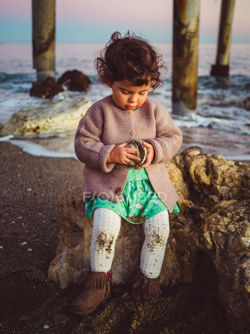 Garoto bonito brincando com concha por um cais na praia — Fotografia de Stock