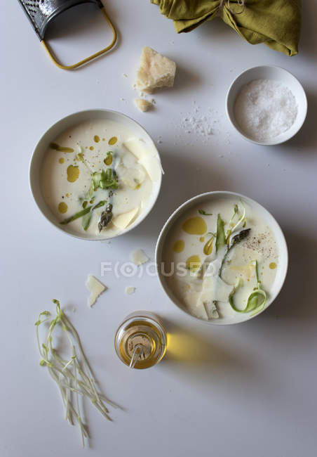 Bowls of yummy asparagus cream soup with cheese and herbs on white background — Stock Photo