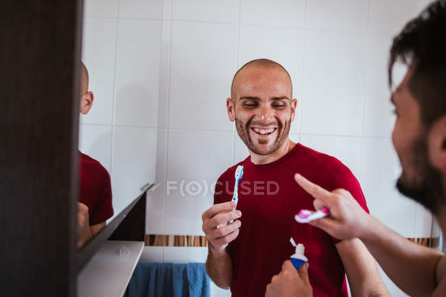 Playful gay couple brushing teeth and fooling around in bathroom — Stock Photo