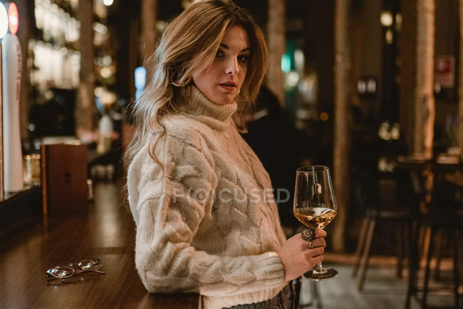 Mulher elegante beber vinho enquanto se inclina no balcão no bar — Fotografia de Stock