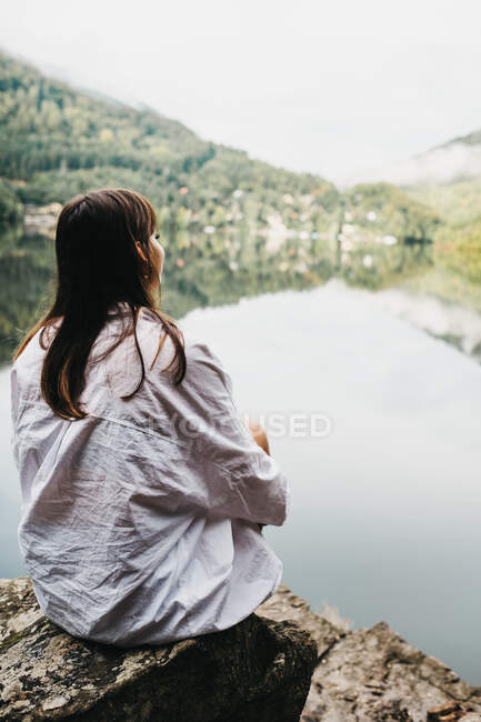Frau sitzt auf Felsen in der Nähe von See und Bergen — Stockfoto