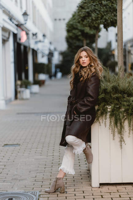 Stylish young woman in vintage leather coat posing on city street — Stock Photo