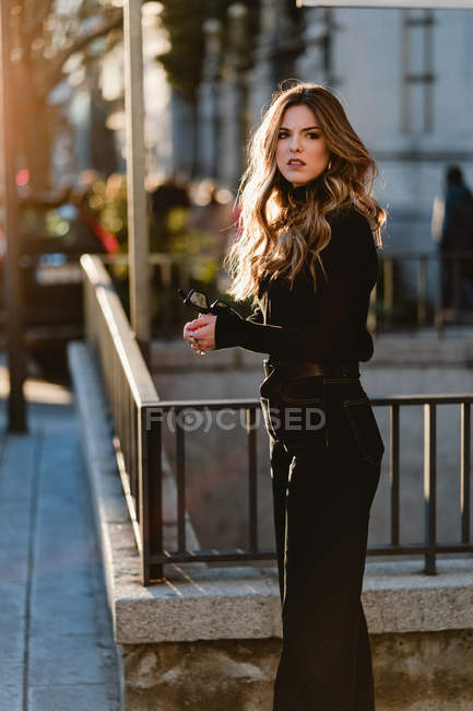 Mujer con estilo de pie cerca de la estación de metro en la calle soleada - foto de stock