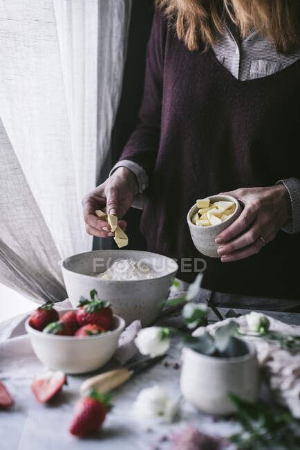 Unrecognizable female adding butter to flour while standing near table and cooking yummy strawberry pastry in kitchen — Stock Photo