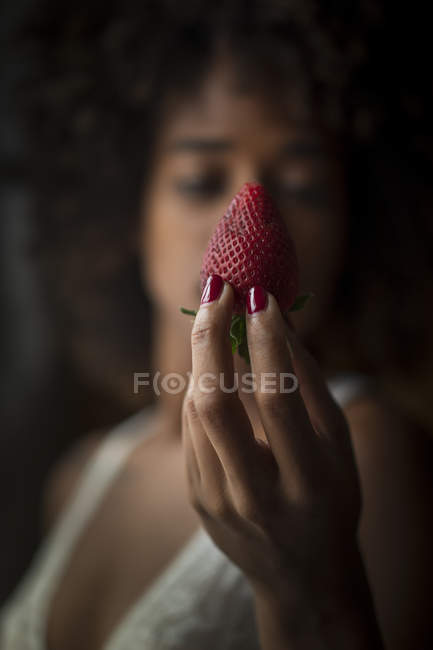 Close-up of woman in bra holding ripe strawberry on black background — Stock Photo