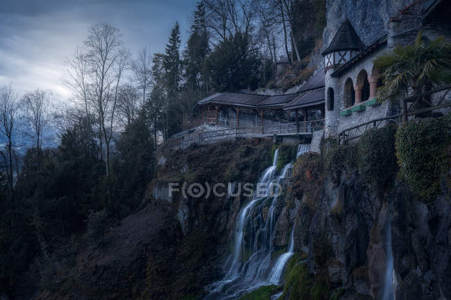 Cascata de água caindo de penhasco rochoso com construção acima, Suíça — Fotografia de Stock