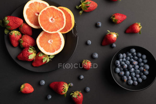 Різні свіжі фрукти та ягоди, розкидані на чорному фоні — стокове фото