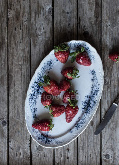 Teller mit leckeren reifen Erdbeeren auf hölzerner Tischplatte in der Nähe von Metallmessern — Stockfoto