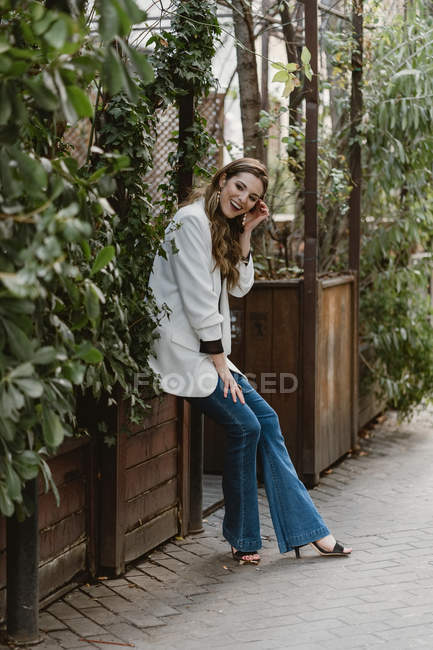 Стильная молодая женщина сидит на плантаторе в саду и смеется — стоковое фото